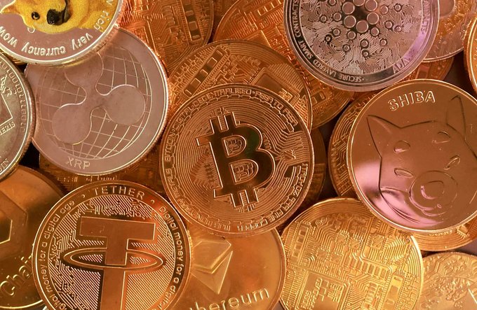 A close-up shows various cryptocurrency coins including Bitcoin, XRP, Tether, Shiba Inu, and Cardano.
