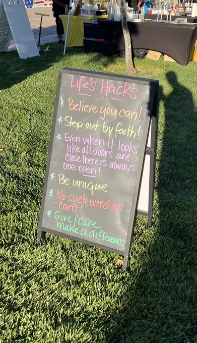 A chalkboard sign on grass titled "Life Hacks" with colorful handwritten tips including "Believe you can!", "Step out by faith!", "Even when it looks like all doors are closed there is always one open.", "Be unique", "No such word as can't!", and "Give / Care make a difference".