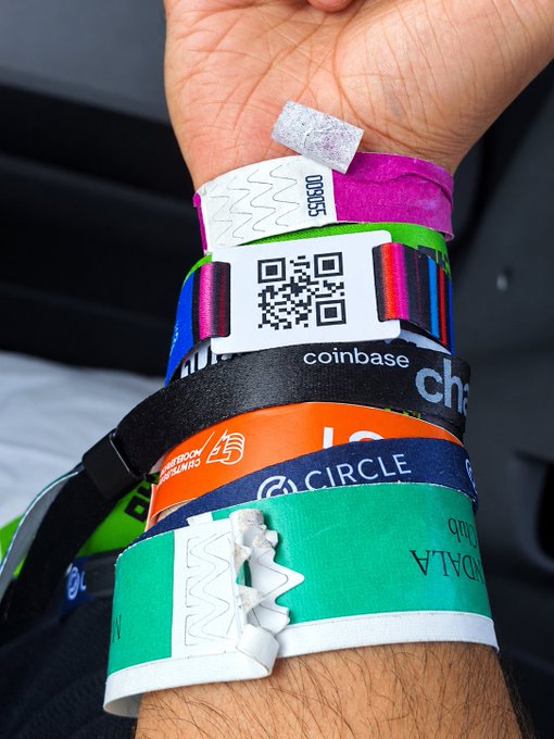 A person's wrist covered in multiple colorful event wristbands with visible text including 'Coinbase', 'CIRCLE', 'COMPASS', '000655', and 'GALAX', displayed as digital materials.