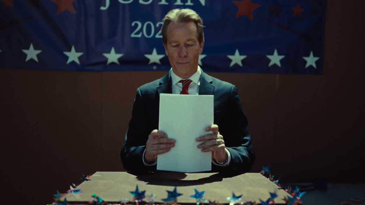 In the image, a man wearing a suit and red tie is sitting at a table with a white sheet of paper in front of him, reading or studying it closely. The man is also holding an important piece of mail that looks like a bill or a newspaper article. There are stars on either side of the frame, possibly representing the American flag. 

In the background, there's a large political sign with the text "$400 duelbits x winify group g&w", which suggests this may be related to the recent presidential election in the United States. The focus is on the man and his interaction with the content of the bill or newspaper article, while also highlighting the larger context of the political scene.