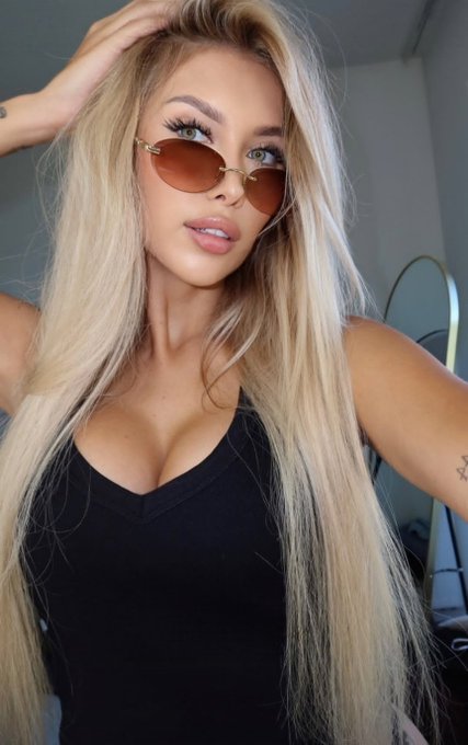 A selfie of a woman with long blonde hair wearing brown tinted sunglasses and a black top, with a small star tattoo visible on her arm.