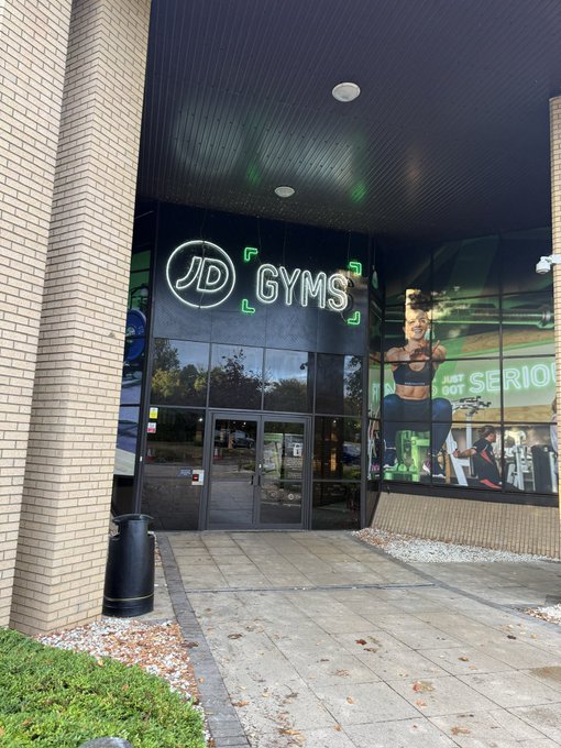 Exterior photograph of a JD Gyms location with a brick facade and illuminated signage above the entrance.