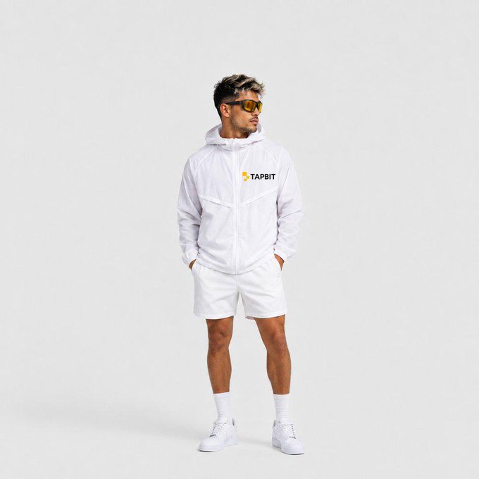 A male model poses in an all-white outfit consisting of a "TAPBIT" branded hoodie, shorts, socks, and sneakers, wearing orange-tinted sunglasses against a plain background.