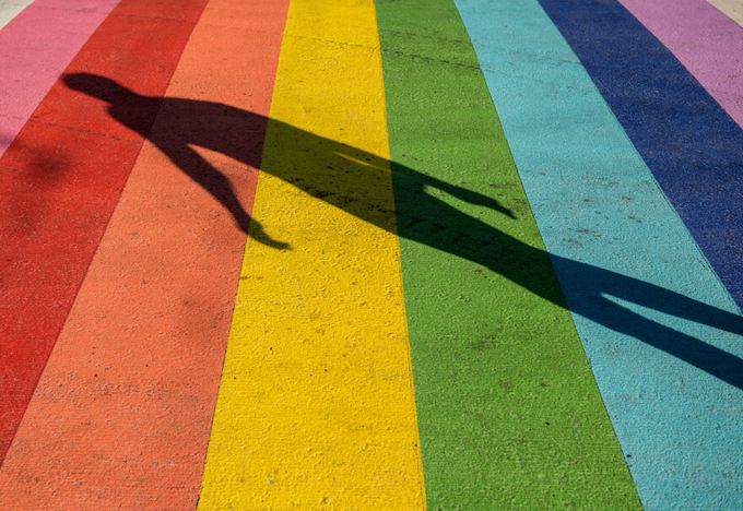 The shadow of a person cast across a rainbow-painted crosswalk.