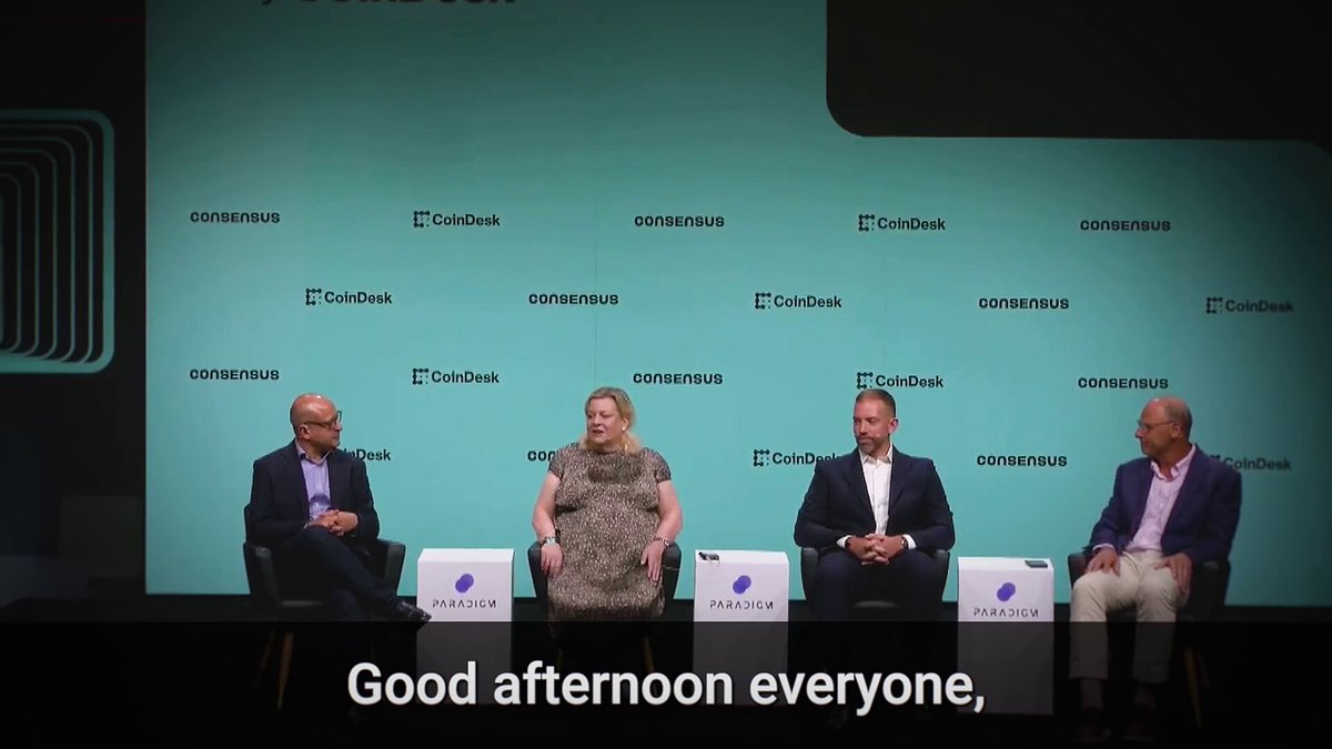 The image shows a group of four people sitting around a table, engaged in conversation or discussion. They are positioned against a backdrop featuring a blue wall with white text that reads "Good afternoon everyone." The individuals appear to be professionals, possibly attending an event or gathering related to data centers and digital asset management.