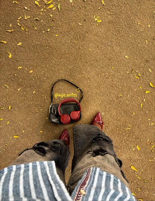 A stylish flat-lay featuring red headphones in a black bag labeled "@ayo.artss," red pointed shoes, and ripped jeans scattered on a leaf-strewn path. The caption hints at the account's NFT success, matching the "@ayo.artss" branding as a signal to potential community members.