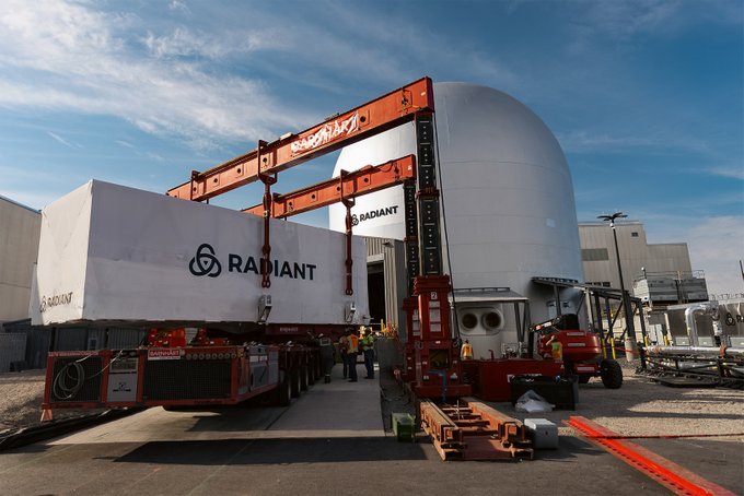 Workers in hard hats operate heavy-lift equipment to position a large white component labeled "RADIANT" near a massive dome-shaped containment structure, likely at a nuclear or industrial facility. The scene captures the precise engineering required to install major reactor components, suggesting the post is commenting on the impressive logistics involved in moving such oversized parts into place.