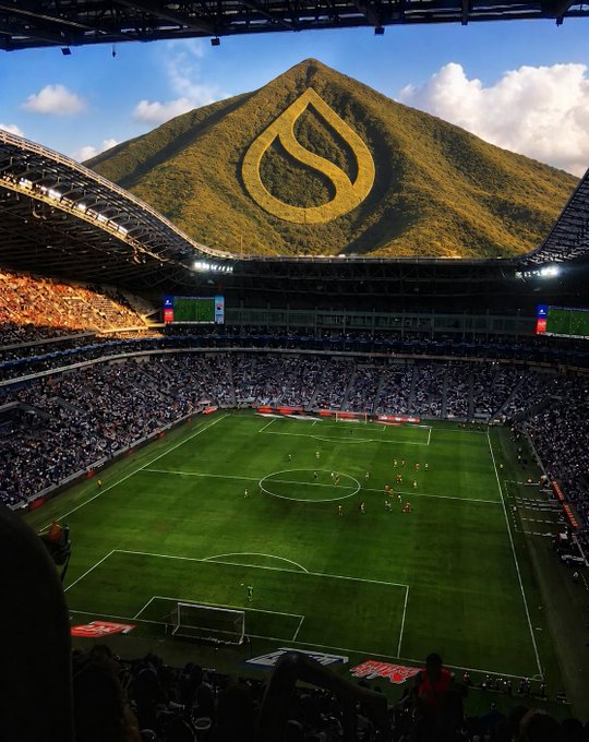 A soccer stadium packed with fans, featuring a digitally edited mountain with a large Sui (water drop) logo behind it.
