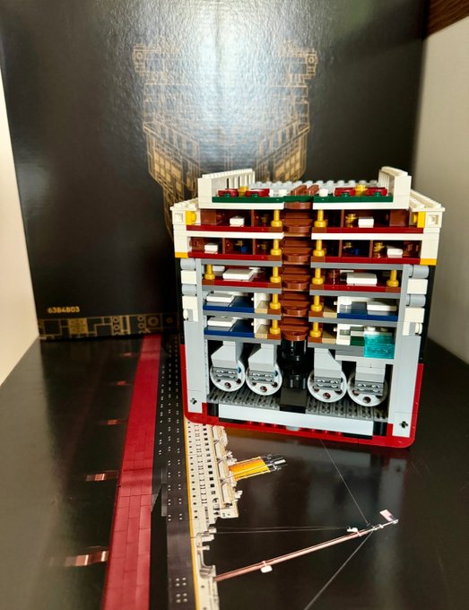 A LEGO cross-section model of the RMS Titanic (#6384803) is displayed with intricate interior details across multiple decks, capturing the complexity the builder mentions about working on "the queen of the ocean." The model's box is visible in the background, showing the set number 6384803, while scattered small LEGO pieces and tools in the foreground reflect the ongoing construction challenge.