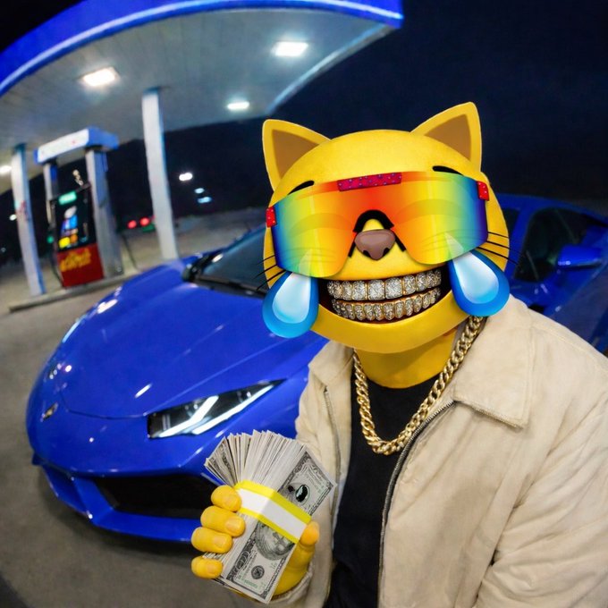 A person wearing a light-colored jacket, a gold chain, and a diamond-encrusted grill poses at a gas station at night, holding a stack of cash in front of a blue sports car, with their face obscured by a cat emoji filter wearing rainbow sunglasses.