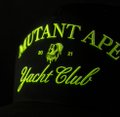 A close-up of a black cap with neon green 'MUTANT APE YACHT CLUB 2021' embroidered text and logo.