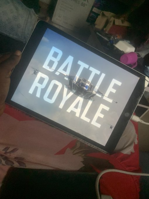 A hand holds a tablet displaying the "BATTLE ROYALE" loading screen, ready to drop into the game.