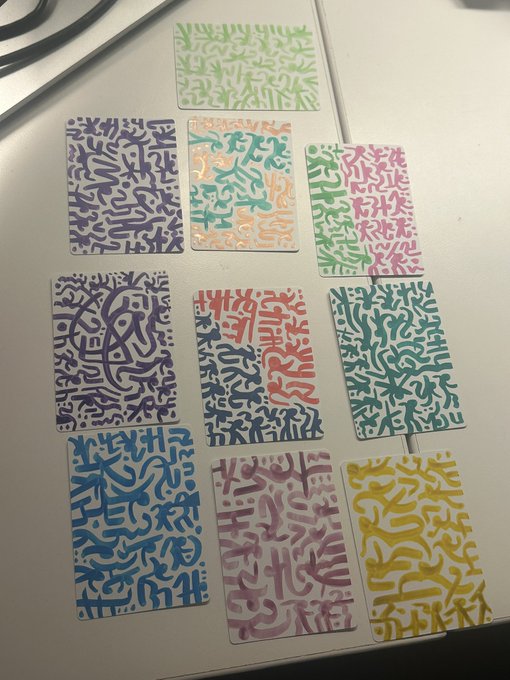 A photograph of nine colorful trading cards arranged on a white surface, each featuring abstract squiggly line patterns in various colors like purple, green, pink, and yellow.