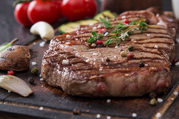 A perfectly grilled steak is seasoned with fresh rosemary, garlic, and peppercorns, served alongside grilled vegetables and tomatoes on a rustic wooden board. This hearty, flavorful dish makes for a satisfying evening meal, fitting the warm sentiment of enjoying a favorite dinner.
