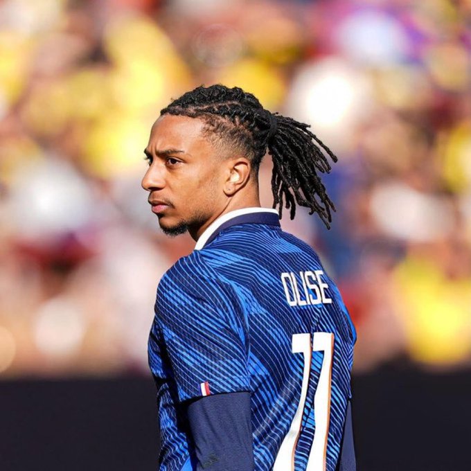 A French national team player wearing jersey number 11 with the name "OLISE" on the back looks over his shoulder, suggesting he is one goal away from another milestone in the match.