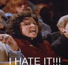The image shows a woman with curly hair sitting among a crowd of people, who are also seated around her. She appears to be making a face or showing some sort of reaction that suggests she is upset or angry about something. The caption below the image reads "I hate it!".