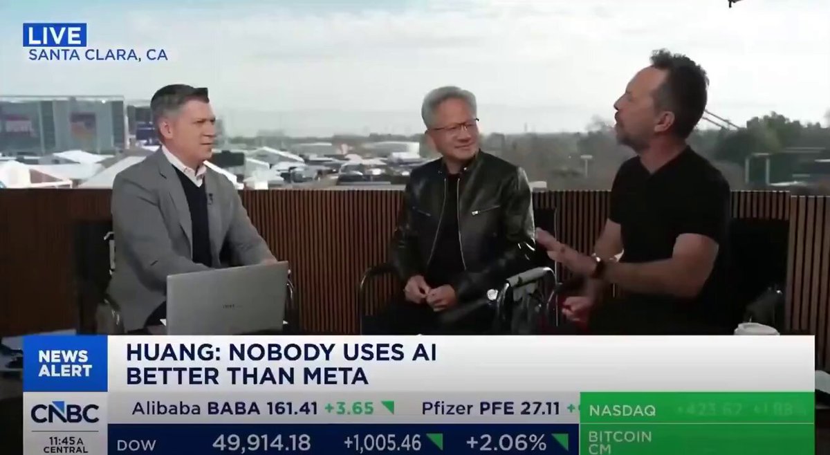 The image is a screenshot of a news story on a television or computer screen about three men sitting at a table with laptops open, watching a video related to artificial intelligence. The headline reads "HUAANG: Nobody uses AI better than Meta". The man in the middle has a laptop and is seated next to another man who seems to be engaged in conversation. A third man sits further back and also has an open laptop. Another person can be seen behind them, but their details are not clear from this image.
