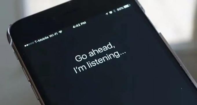 A smartphone screen displays the message "Go ahead, I'm listening..." with a T-Mobile Wi-Fi connection at 4:42 PM, suggesting the use of a voice assistant like Siri. The image ties into the post by visually representing the convenience and prevalence of AI voice assistants, implying that not using one would be "madness."