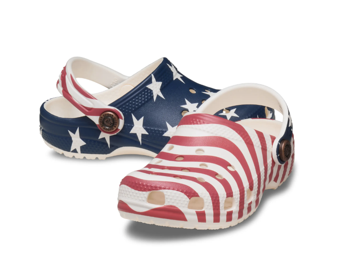 A pair of classic clog-style shoes decorated with an American flag pattern of stars and stripes is displayed against a white background.