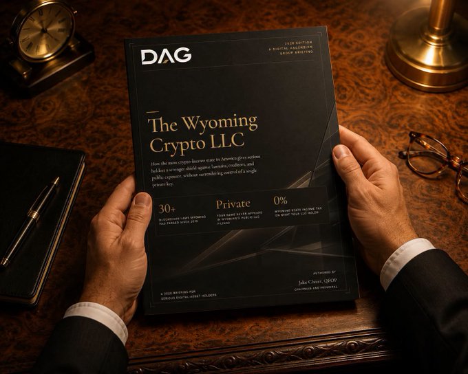 A person in a suit holds a black brochure titled "The Wyoming Crypto LLC" by DAG Digital Asset Group, sitting on a wooden desk beside a leather notebook, pen, and brass lamp. The image visually reinforces the post's promotion of a free briefing on using Wyoming-based LLCs for legal crypto ownership, asset protection, and tax-efficient wealth structuring.