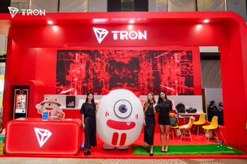 A promotional TRON booth featuring red branding, a large mascot character, and two women posing in front of a digital display.