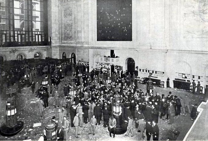 A black and white historical photograph of a crowded trading floor, likely the New York Stock Exchange, with many men in suits gathered around.