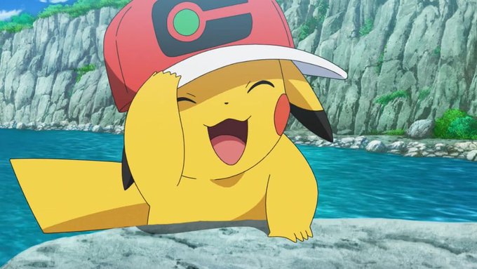 A still from the Pokémon anime showing Ash Ketchum's Pikachu wearing a red cap and laughing joyfully on a rocky shore beside water.
