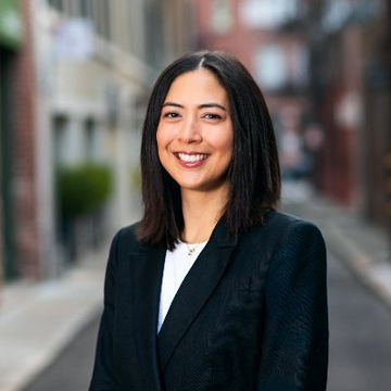 The image shows a professional woman with shoulder-length dark hair, smiling at the camera while wearing a dark blazer over a white top, with a blurred urban street background suggesting a city setting.

The post connects to the image as the woman pictured appears to be Monica Long, the Ripple executive referenced, who recently outlined the company's vision for multichain, interoperable payment infrastructure powered by institutional-grade blockchain technology, positioning XRPL as a hub for regulated stablecoins like RLUSD alongside XRP.