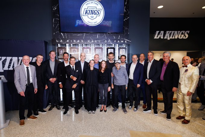 A group of formally dressed individuals poses together at the unveiling of the LA Kings Hall of Fame installation at Crypto.com Arena, with the "KINGS SINCE 1967" logo and "LA KINGS HALL OF FAME" display visible in the background. The gathering celebrates the first 60 years of Kings history, honoring the franchise's notable players, staff, and broadcasters whose portraits are featured on the wall behind them.