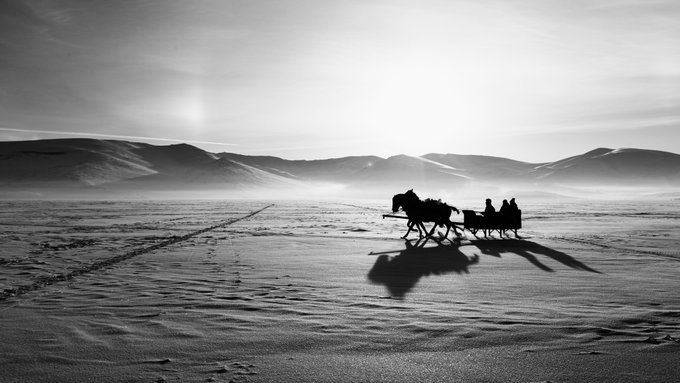A monochromatic silhouette captures a horse-drawn sleigh carrying figures across a vast, snow-covered landscape with rolling hills, evoking the tranquil finality of "Sleigh Ride at Sunset." The piece, posted as the artist's "last piece" on @objktcom, reflects a farewell message through its serene, almost ghostly scene of a journey ending at dusk.