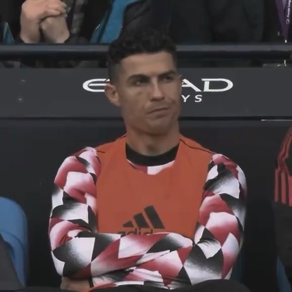 Cristiano Ronaldo sitting on a bench wearing an orange and patterned Adidas training top, with an 'Etihad' sponsor sign visible behind him.