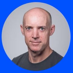 Profile photo of a bald man wearing a dark gray t-shirt against a light gray background with a blue border.