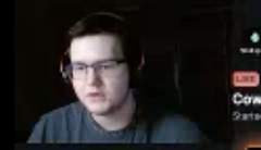 A blurry webcam photo of a young man with glasses, appearing to be a streamer with a 'LIVE' indicator and partial text 'Com' and 'Game' visible on the side.