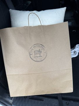 A tan paper bag from "The Woolshire" rests on a car seat with a white pillow visible inside, showing the recent purchase made at the Modern Homesteading conference and paid for with Bitcoin through the AquaBitcoin Wallet.