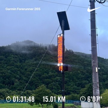 A Garmin Forerunner 265 screen captures a digital sign in Japan showing '猛暑警戒' with stats 01:31:48, 15.01 KM, and 6'07" pace against a misty mountain backdrop.