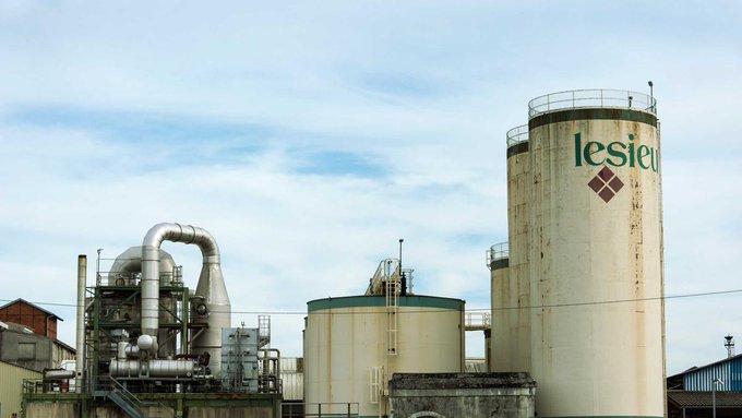 An industrial facility with silos labeled 'lesieur' alongside processing equipment under a partly cloudy sky.