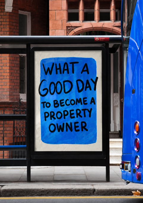 An advertisement on a bus stop displays the handwritten message "WHAT A GOOD DAY TO BECOME A PROPERTY OWNER" on a blue background.