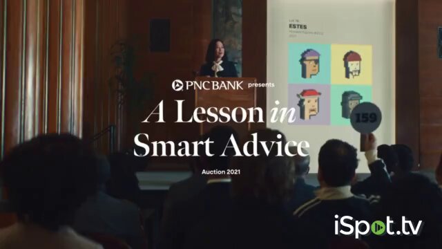 The image features an advertisement for PNC Bank's "A Lesson in Smart Advice". The background of the ad shows a woman giving a presentation, with a projector displaying a slide that says "A Lesson in Smart Advice" on it. There are several people sitting and watching the presentation from various positions around the room.

The text in the image reads: "Our JPEGs are back on TV screens, except this time it' s a @PNCBank ad gently roasting us @cryptopunks in primetime, courtesy of a bank's Smart Advice". The post also mentions that PNC Bank is presenting at an auction event.