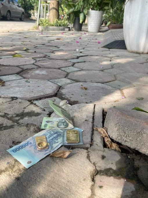 Several Indonesian rupiah banknotes, including a 50,000 denomination, lie on a paved outdoor walkway scattered with leaves.