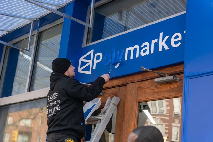 A worker installs a "Polymarket" sign at a storefront entrance, symbolizing the company's physical presence just as France's gambling regulator ANJ orders telecom providers to block the platform, classifying it as an illegal gambling service amid concerns over weather bets and potential data manipulation.