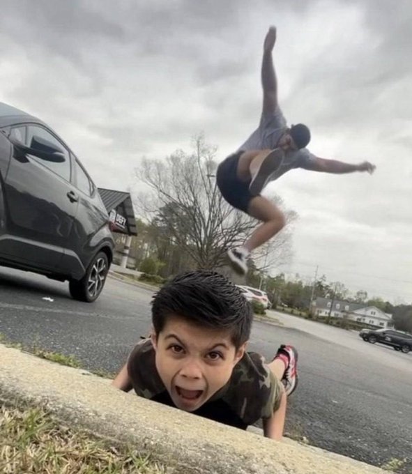 A man with an excited, wide-eyed expression pops up from below a curb while another person leaps dramatically over him in mid-air, with a black SUV parked on the street behind them. The image humorously captures the exuberant, over-the-top energy of crypto enthusiasts celebrating on-chain activity, mirroring the chaotic joy referenced in the caption about Bitcoin sellers being startled by traders finally having fun after months of inactivity.
