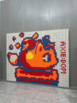 A large pixel art mosaic of the Axieboom logo featuring a red character on a white background, leaning against a gray wall.