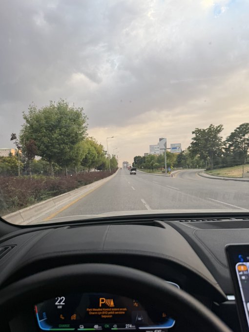 A driver's perspective view from inside a car traveling on a multi-lane road, showing the dashboard displaying parking sensor alert 'Park-Meidau kontroll ezker alde' with a speed of 22 and temperature of 27°C.