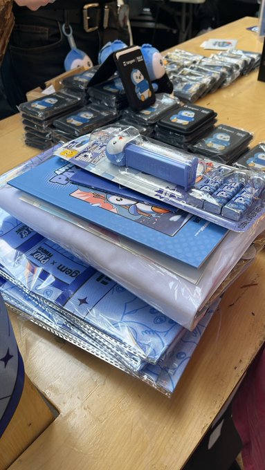 Photo of merchandise laid out on a wooden table, including blue-themed stationery, Doraemon-themed accessories, and packaged goods.