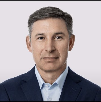 A professional headshot of a man in a blue suit jacket and light blue shirt.