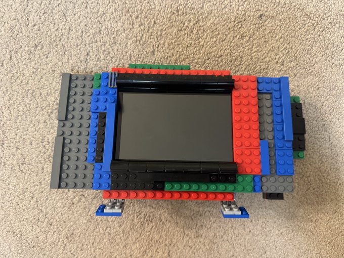 A Nintendo Switch console encased in a colorful Lego brick cover sits on a beige carpet.