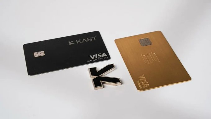 The image features two credit cards, one black and one gold, placed next to each other with a small magnet attached to them. The magnets are shaped like letters "K" and "Visa", indicating their respective brands. The text on the magnets reads "@KAST xyz". This suggests that these credit cards might be from KAST or Visa, as they have been magnetized to display their logos prominently.