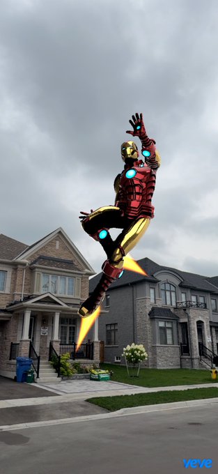 An AI-edited image showing Iron Man flying above suburban houses with jet boosters, branded with the 'xove' watermark.