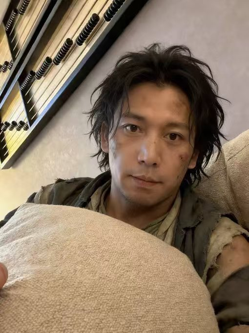 Selfie of a man with messy dark hair and dirt-smudged face, wearing tattered clothing, with pool cues visible in the background.