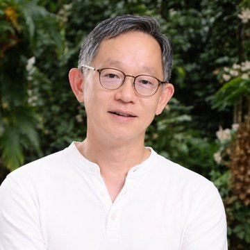 A middle-aged Asian man with short dark hair and round tortoiseshell glasses, wearing a white henley shirt, is photographed outdoors against a backdrop of lush green foliage. His image accompanies the announcement that Evan (@evanweb3), co-founder of SUI, has taken on a leadership role at Mysten Labs, marking a significant shift for the Sui Network's future direction.
